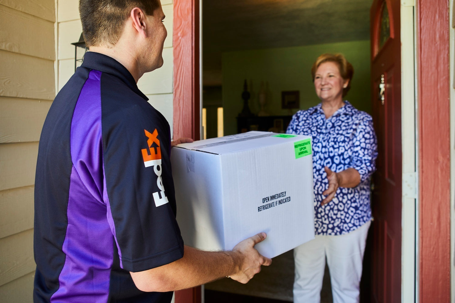 FedEx delivery person handing a package to a customer at a door.
